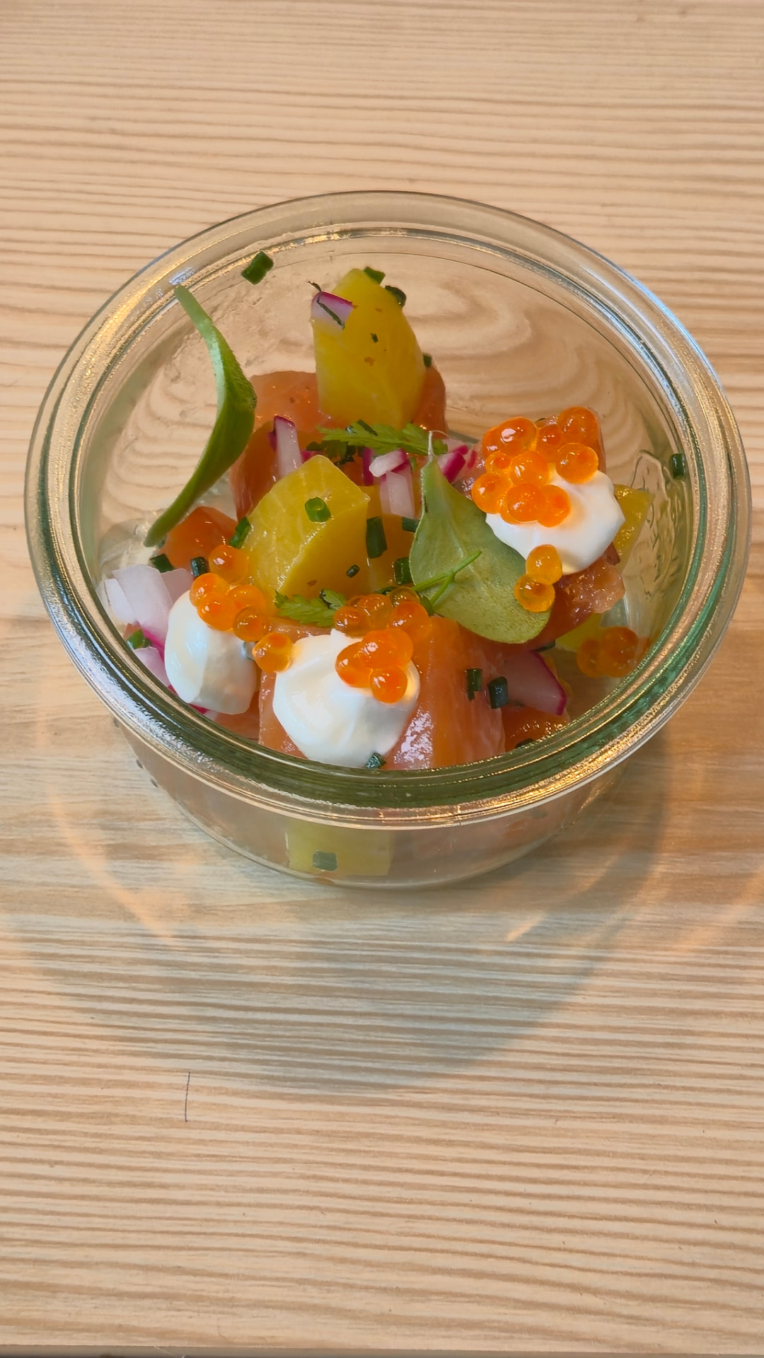 Fingerfood mit Lachs, Gemüse, Kräutern und kleinen Perlen in einem Glas.