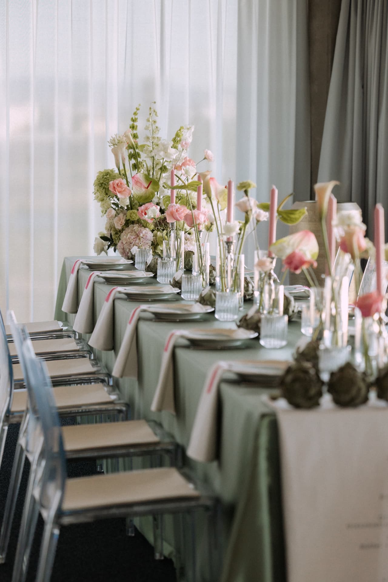 Lange Hochzeitstafel im Circle Cube mit salbeigrüner Decke, rosa Kerzen und Blumenarrangements vor bodentiefen Fenstern